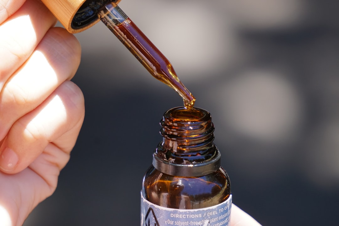 Hand holding CBD oil dropper above bottle