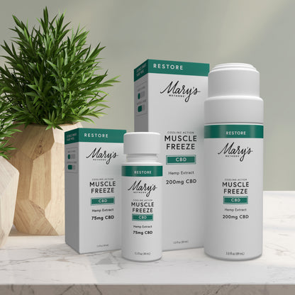 Mary's Methods Muscle Freeze CBD products on a white surface with a plant in the background.