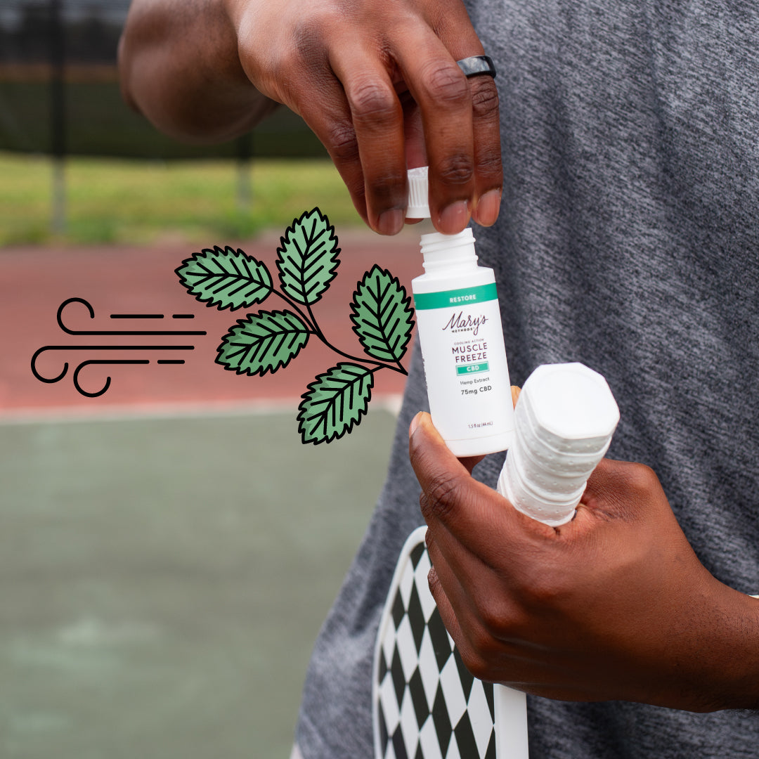 Person holding Mary's Methods Restore CBD Muscle Freeze with green leaves and pickleball paddle.