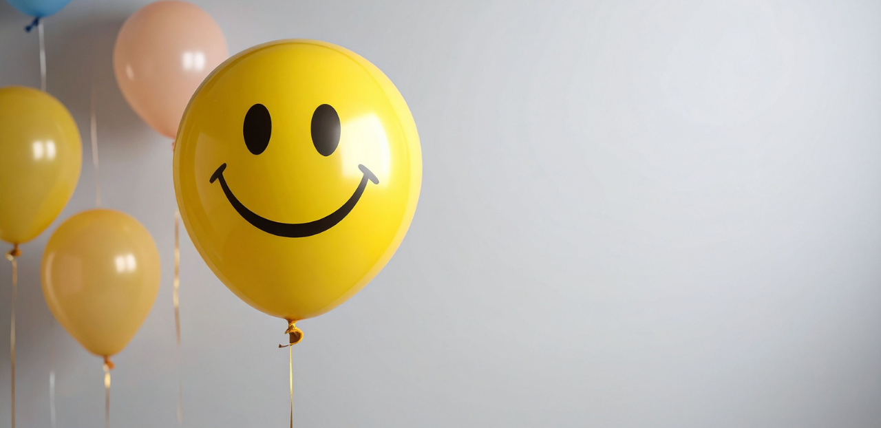 Yellow balloon with a smiley face design among other balloons against a light gray background